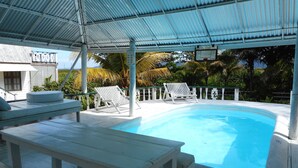 A pool area with a covered patio, lounge chairs, and a bench. - Chippewa Village Pool Apt  (Negril)