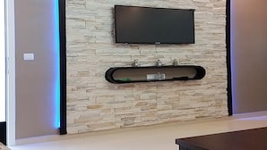 A modern living room with a stone wall, a mounted flat-screen TV, and a black entertainment unit. - Great Pool View Apartment in Kariat Cabo 4548 (Cabo Negro)