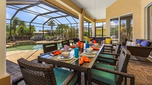 Un espace extérieur aménagé pour les repas, doté d'une structure vitrée, de mobilier en osier et d'une piscine.