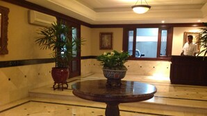 A lobby with a marble floor, a round wooden table with a plant, and a reception desk.