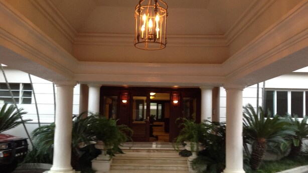 A covered entrance with a chandelier, columns, and potted plants.