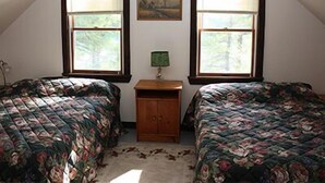 A bedroom with two beds, a nightstand, a painting, and two windows with blinds. - Water Front Cape Style Cottage (Oxford)