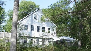 A two-story house with a gabled roof, surrounded by trees and a wooden fence. - Water Front Cape Style Cottage (Oxford)