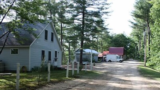A rural road with a white house and a truck parked on the side. - Water Front Cape Style Cottage (Oxford)