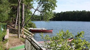 A wooden dock extending into a lake with a red boat moored at the end. - Water Front Cape Style Cottage (Oxford)