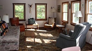 A cozy living room with a fireplace, comfortable seating, and large windows. - Water Front Cape Style Cottage (Oxford)