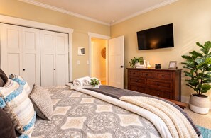 Une chambre à coucher avec un lit, une commode, un téléviseur et une plante en pot.