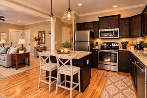A modern kitchen with dark wood cabinets, stainless steel appliances, and a marble countertop island with two bar stools. - Private Hot Tub & Fireplace, 2 Miles from Asheville (Asheville)
