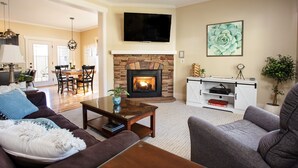 A living room with a fireplace, a television mounted above it, and a dining area in the background.