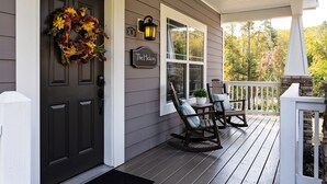 A porch with a dark door, a wreath, a sign reading "The Hickory," and two rocking chairs.