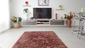 Un salon moderne doté d’un téléviseur à écran plat, d’un meuble de rangement en bois, de plantes décoratives et d’un tapis moelleux.