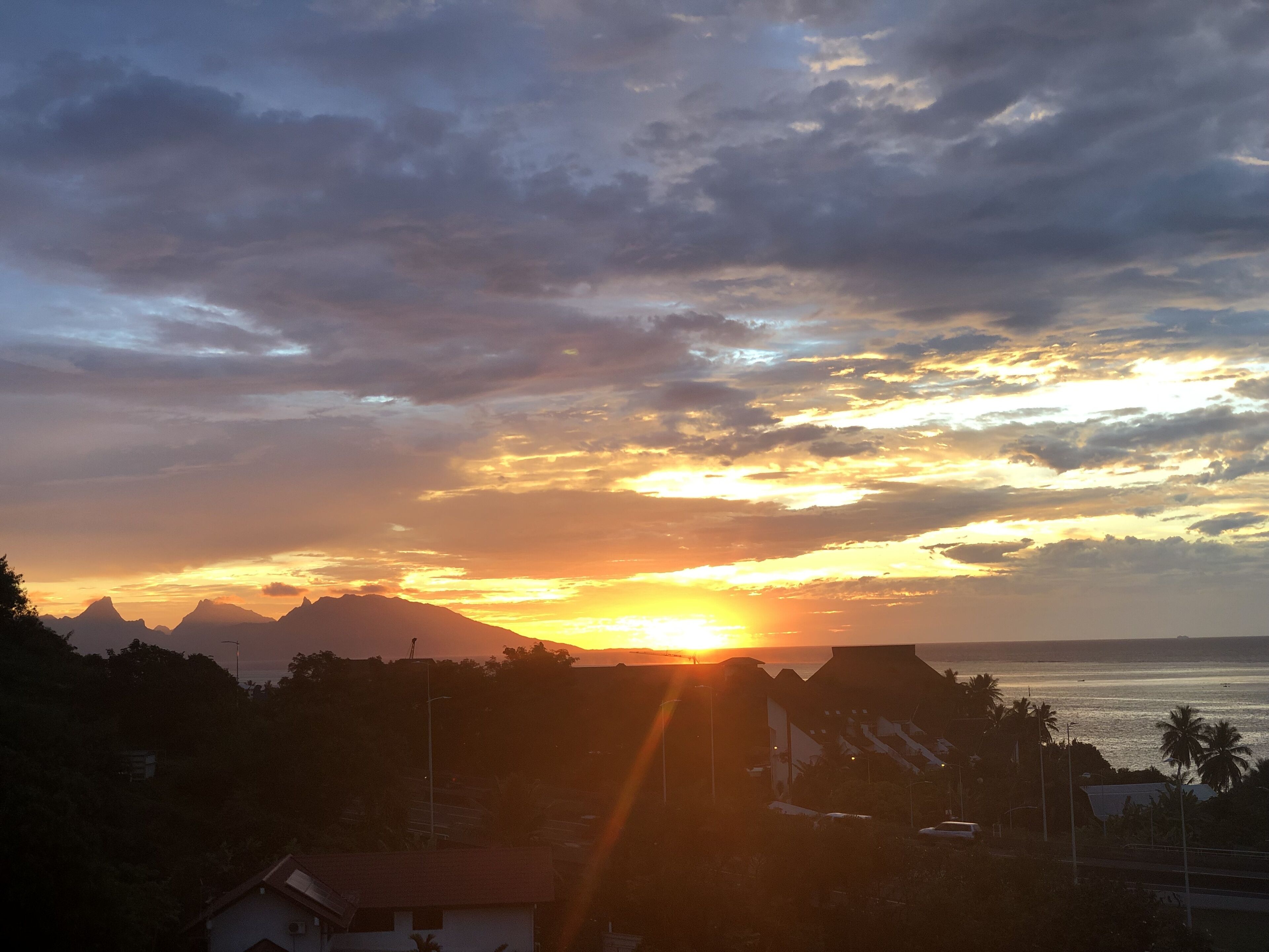 A sunset over mountains with a view of the ocean and residential buildings.