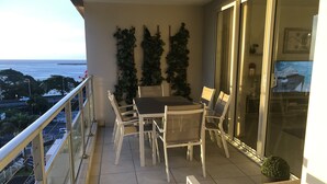 Un balcon avec une table et des chaises, une plante en pot et une vue sur l’océan.
