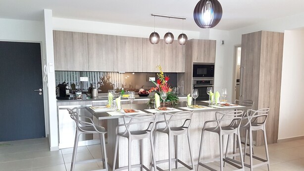 Une cuisine moderne avec des tabourets de bar gris, une table à manger dressée pour six personnes et un élément décoratif central.