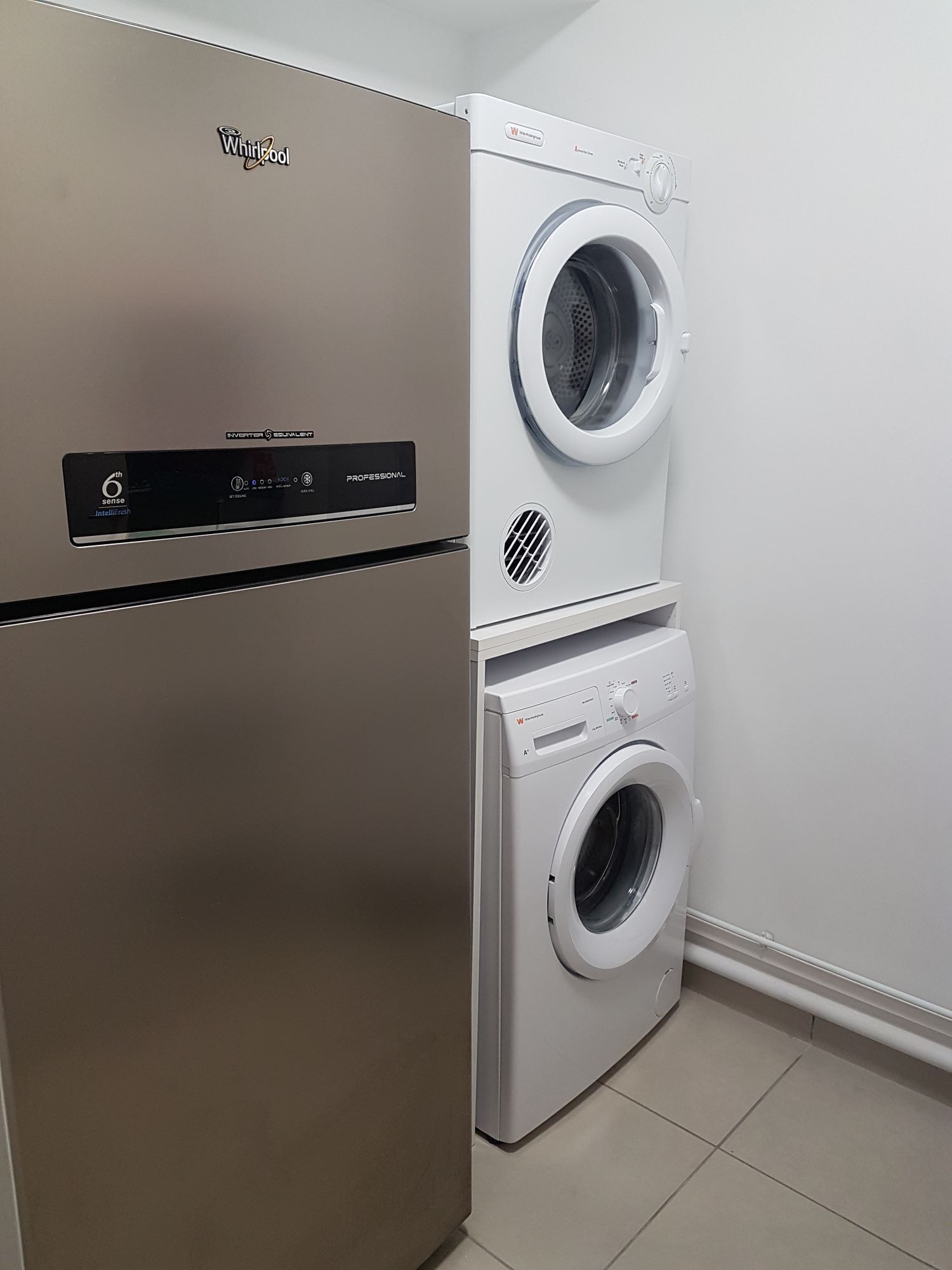 A Whirlpool washer and dryer unit in a clean, modern laundry room with a stainless steel refrigerator.