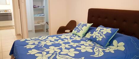 A bedroom with a bed, a brown upholstered headboard, and a wardrobe with shelves.