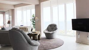 A modern living room with a grey sofa, armchair, and a round coffee table. A flat-screen TV is mounted on the wall.