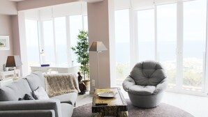 A living room with a grey armchair, a sofa, and a coffee table. There is a large window with a view of the city.