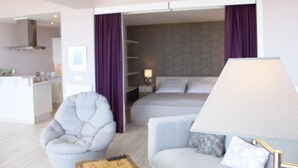 A modern hotel room with a bed, two armchairs, a sofa, a lamp, and a small table.