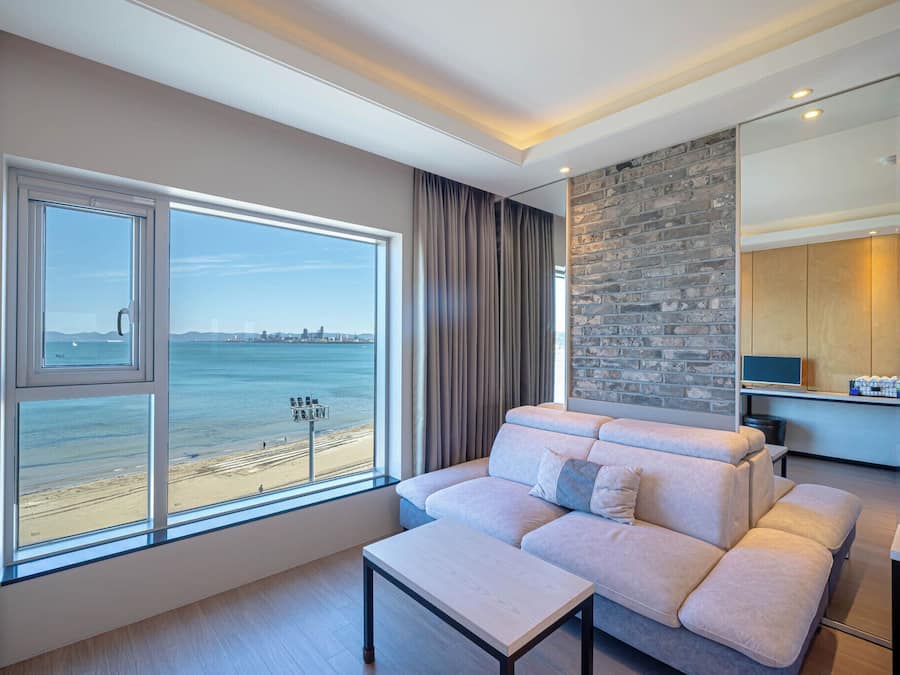A modern living room with a large window overlooking a beach, a sofa, a small table, and a brick accent wall.
