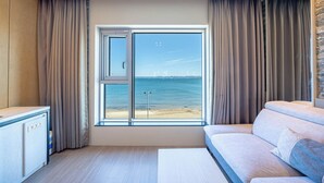 A modern room with a large window offering a view of the sea and distant ships. - Pohang Yeongildae Hotel View (Pohang)
