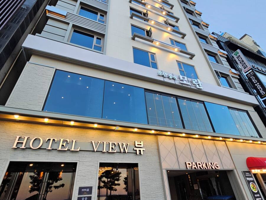 Ein mehrstöckiges Hotelgebäude mit einem gut sichtbaren Schild 'HOTEL VIEW' im Erdgeschoss, einem 'PARKING'-Schild und einem modernen architektonischen Design mit großen Fenstern und Balkonen.