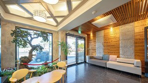 A reception area with a wooden ceiling, a large tree, and a sofa with cushions. - Pohang Yeongildae Hotel View (Pohang)