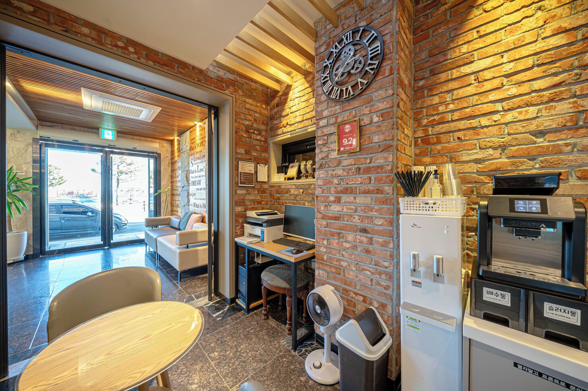 Een modern interieur met een bakstenen muur, een grote klok, een receptiebalie, een zithoek en een koffieapparaat.