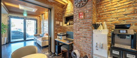 A modern interior with a brick wall, a large clock, a reception desk, a seating area, and a coffee machine.
