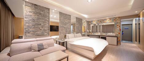 Une chambre d’hôtel moderne dotée d’un grand lit, d’un canapé, d’une petite table, d’une salle de bain avec douche et d’un coin cuisine.