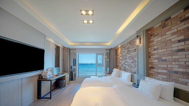 A modern hotel room with a large bed, a flat-screen TV, a desk with a computer, and a brick accent wall. - Pohang Yeongildae Hotel View (Pohang)