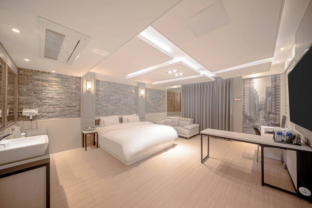 A modern hotel room with a large bed, a desk, a vanity, and a city view.