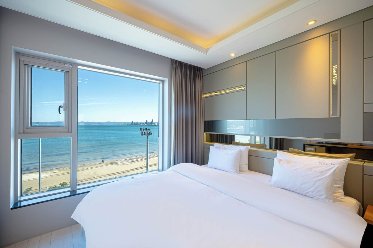A hotel room with a large bed, a view of the beach, and a cityscape.