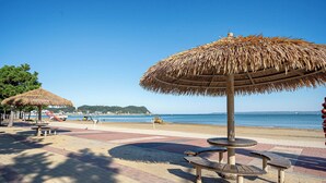 A beachside walkway with thatched umbrellas and picnic tables. - Pohang Yeongildae Hotel View (Pohang)