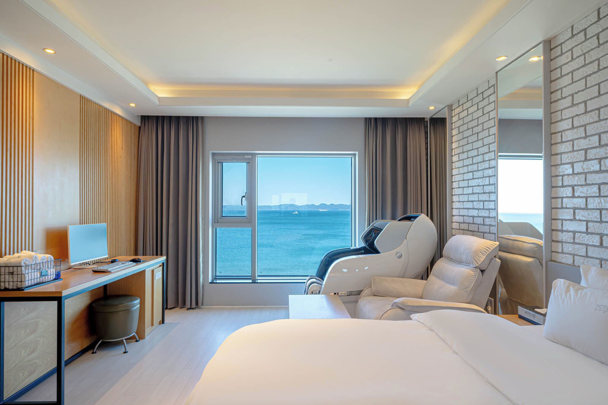 Habitación de hotel moderna con una cama grande, un escritorio con computadora, una silla de masaje y vistas al mar.
