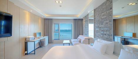 Ein modernes Hotelzimmer mit einem großen Bett, einem Schreibtisch, einem Flachbildfernseher und Blick aufs Meer.