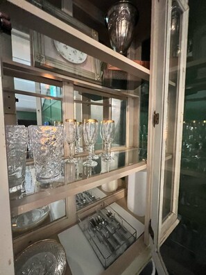 Un escaparate de vidrio con diferentes vasos y una bandeja metálica con utensilios.