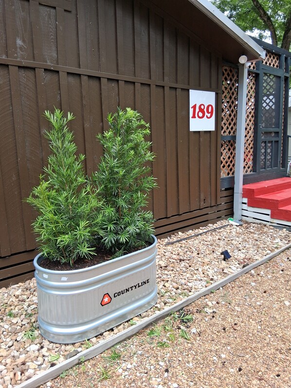 Una jardinera de metal con dos plantas en macetas frente a una valla de madera con un letrero que dice "189".