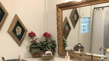 A bathroom with a large mirror, a white sink, and a wooden vanity. There are decorative baskets and a small stool.