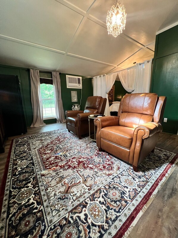 Una sala de estar con un tapete grande de diseño, dos sillones de cuero, una araña y una pared verde.