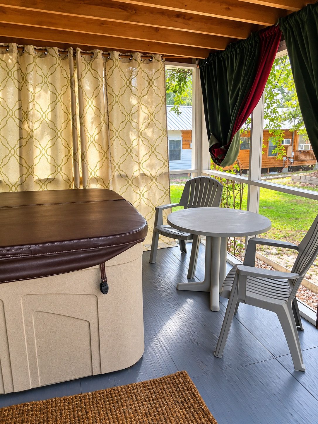A covered outdoor seating area with a table and chairs, a bench, and a view of the backyard.