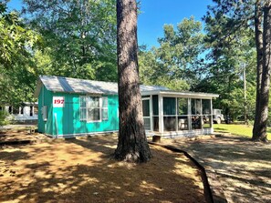 A small, single-story building with a green exterior and a white porch. - COZY OVERNIGHT STAY WITH PRIVATE HOT TUB. OLD MILL VILLAGE CABIN 197 (Kennard)