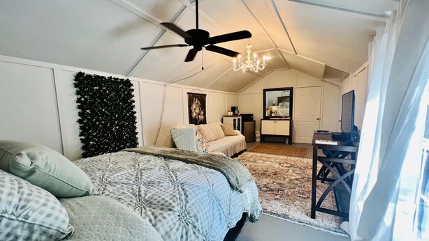 A bedroom with a bed, a ceiling fan, a chandelier, a desk, and a mirror. - CUTE CABIN, PRIVATE HOT TUB, QUEEN BED, SMALL TOWN, 4 MILES TO RATCLIFF LAKE (Kennard)