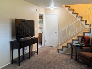 A living room with a TV, a console table, a staircase, and a chair.