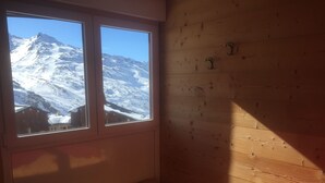 A room with wooden walls, a window with a snowy mountain view, a wooden bench, and a red chair.