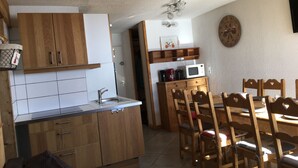 A compact kitchen with wooden cabinets, a sink, and a dining area with wooden chairs.