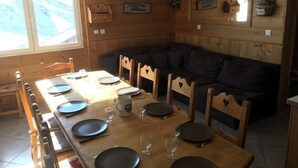 A wooden interior with a dining table set for four, a dark-colored sofa, and a window with a view.