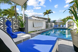 A pool area with lounge chairs, a palm tree, and a building in the background. - one bedroom furnished apartment by beach (West Palm Beach)