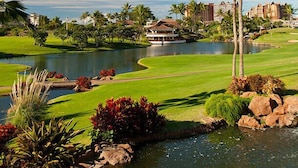 Un campo de golf con un estanque, palmeras y un edificio con techo blanco.
