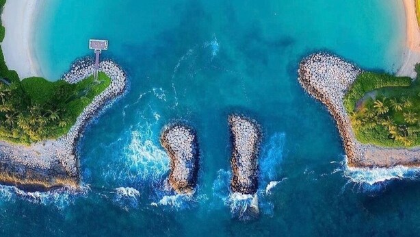 Vista aérea de un resort en la playa con una extensa playa de arena, aguas turquesas cristalinas y un pequeño muelle.